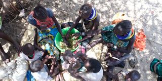 A woman and children eat wild leaves in Kanamkuny village in Turkana County