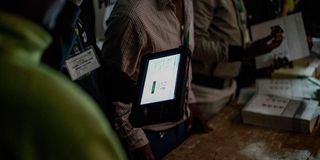 An IEBC official verifies a voter's details on the Kenya Integrated Electoral Management System (KIEMS) kit